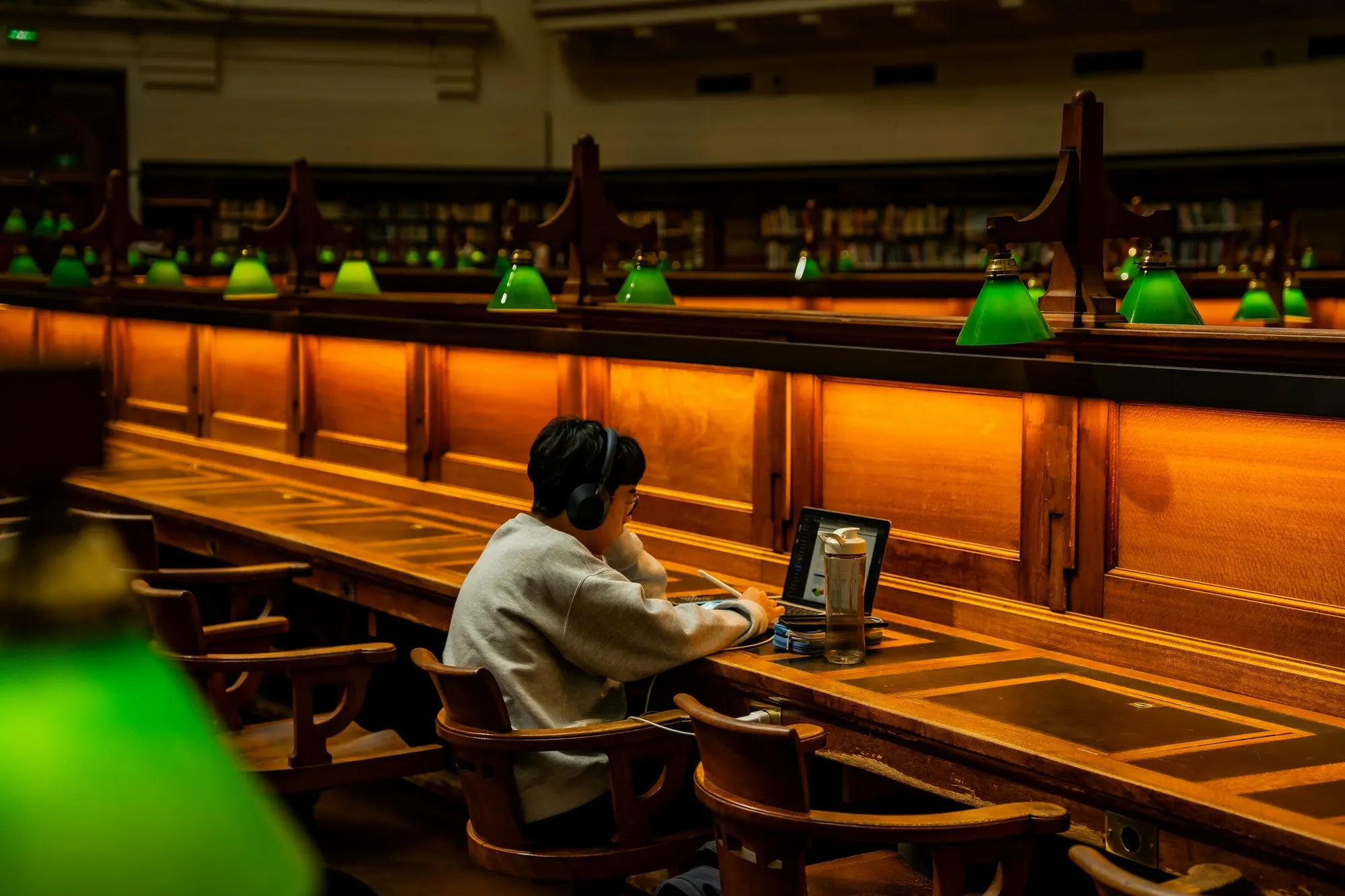 A student working alone in a library lit by green lamps